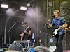 To musikere spiller elektrisk gitar på en scene med mikrofoner, scenelys og røyk.