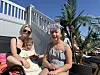 Tre personer sitter i solen ved et basseng med palme og hvit rekkverk i bakgrunnen.