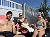 Fire personer sitter i solstoler ved et utendørs basseng med palmer og hvite gjerder.