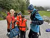 Flere personer i turklær står på en steinstrand med en sekk og en bøye i forgrunnen.