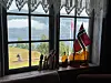 Et vindu med utsikt mot fjord og fjell, med norsk flagg, flasker og små trefigurer i karmen.
