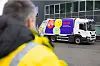 En renovasjonsbil med fargerik dekor står ved en bygning, sett forbi en uskarp person i gul jakke.