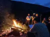 Flere personer samles rundt et stort bål ute i mørket, med fjell som bakgrunn.