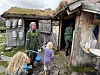 Tre personer står ved inngangen til en værbitt seterbygning med gress på taket og bøtter på veggen.
