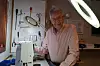 En mann står i et verksted med symaskin, verktøyoppheng og sterke arbeidslamper.