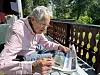 En eldre mann sitter på en terrasse og leser en avis i solskinn.