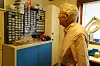 En eldre mann står i et kjellerverksted med hyller fulle av små plastbokser og arbeidsbenk.