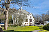 Hvit villa med rødt detaljerte balkonger, trær og grønt gress i solskinn.