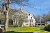 Hvit villa med rødt detaljerte balkonger, trær og grønt gress i solskinn.