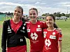 Tre unge fotballspillere i røde og svarte drakter står sammen på gressbanen.