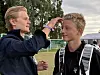 To ungdommer står ved en fotballbane, og den ene retter håret til den andre.