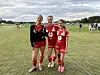 Tre unge fotballspillere i røde drakter står side om side på en gressbane.