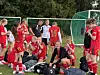 En gruppe unge fotballspillere i røde drakter samles på gresset foran mål og nett.