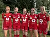 Fem ungdomsspillere i røde fotballdrakter står på rekke utendørs foran trær.