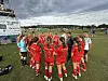 Ungdomsspillere i røde drakter står i en sirkel på en fotballbane med en trener i midten.