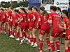 En gruppe jenter i røde fotballdrakter står samlet på en gressbane før kamp.