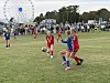 To jentelag spiller fotball på en gressbane, med tilskuere og et pariserhjul i bakgrunnen.