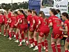 En rekke unge fotballspillere i røde drakter står samlet på gresset ved sidelinjen.