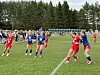Ungdomsspillere i røde og blå drakter kjemper om ballen på en gressbane.