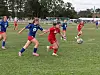 Ungdomsspillere i røde og blå fotballdrakter kjemper om ballen på en gressbane.