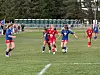 Ungdomsspillere i røde og blå fotballdrakter løper etter ballen på en gressbane.