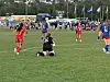 Ungdomsseriespillere i røde og blå drakter spiller fotball på en gressbane.