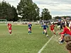 Fotballkamp på gressbane med spillere i røde og blå drakter og publikum langs sidelinjen.