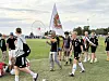 Fotballspillere i svarte drakter samles og feirer på en gressbane med en flaggbanner i bakgrunnen.