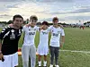 Fire fotballspillere står side om side på en gressbane med mål og et pariserhjul i bakgrunnen.