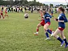 To fotballspillere i blå drakter løper mot en ball mens en spiller i rødt nærmer seg på gressbanen.