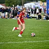 Fotballspiller i rødt løper med ballen på en gressbane mens tilskuere ser på i bakgrunnen.