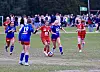 Flere unge fotballspillere i røde og blå drakter løper etter ballen på en gressbane.