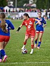 Ungdomsspillere i rødt og blått konkurrerer om ballen på en gressfotballbane.