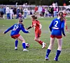 Tre unge fotballspillere kjemper om ballen på en gressbane, med publikum i bakgrunnen.