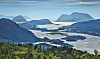 Panoramautsikt over fjord med øyer, fjell og skogkledd forgrunn under klar himmel.