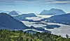 Panoramautsikt over fjord med øyer, fjell og skogkledd forgrunn under klar himmel.