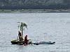 To personer står på en liten flåte med vannsportsutstyr ved vannkanten.