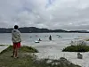 En person står på stranden og ser ut over havet der flere driver vannsport under en overskyet himmel.