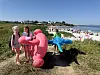 Barn står ved rosa og blå oppblåsbare figurer ved en sandstrand med mange badende i bakgrunnen.