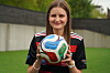 En ung kvinne står på en fotballbane og holder en ball foran seg med begge hender.