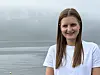 En smilende ung kvinne står foran et stille sjølandskap.