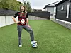 En kvinne står på en kunstgressbane i en hage med en fotball under foten.
