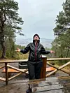 Person på en treplattform i regnvær med armene utstrakt foran skog og fjell.