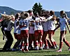 En gruppe fotballspillere i hvite og røde drakter står i en tett ring på en gressbane.