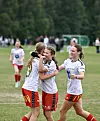 Tre fotballspillere i hvite trøyer og røde shorts feirer med en klem på gressbanen.
