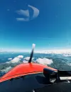Utsikt fra cockpiten i et småfly over skyer og landskap, med propell og rød nesedel i forgrunnen.