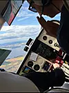 Utsikt fra innsiden av et småflycockpit med instrumentpanel, pilot og landskap sett gjennom frontruten.