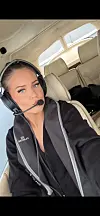 En kvinne med headsett sitter i cockpit i et lite fly med beige seter.