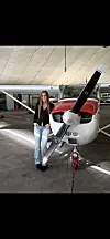 Ung kvinne står ved siden av et rødt og hvitt småfly i en hangar.