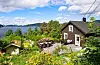 Enebolig med terrasse og frodig hage med utsikt mot fjorden og øyer i bakgrunnen.